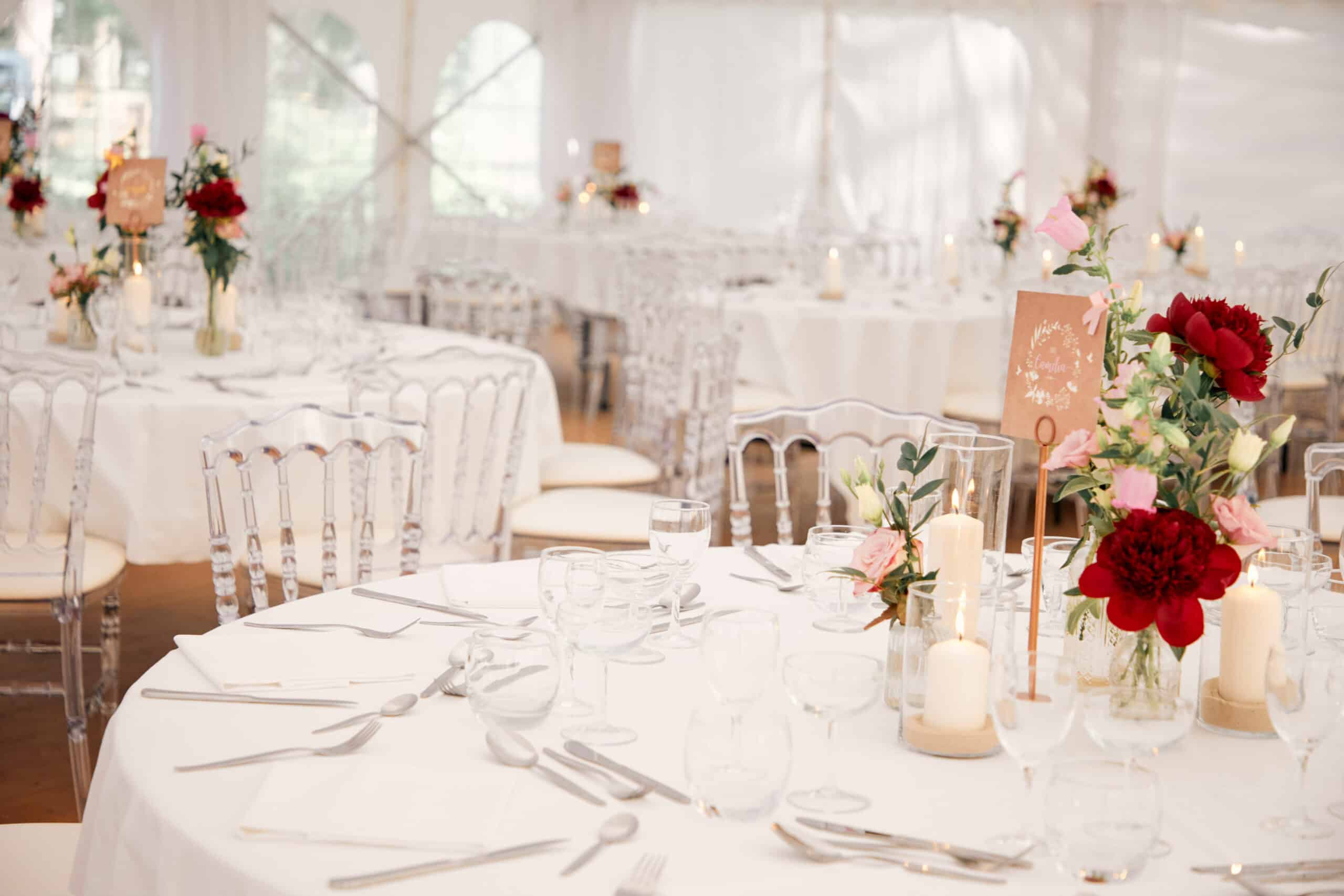 Tables nappée en blancs comportant de la vaisselle, des bougies et des bouquets de fleurs dressées pour un mariage